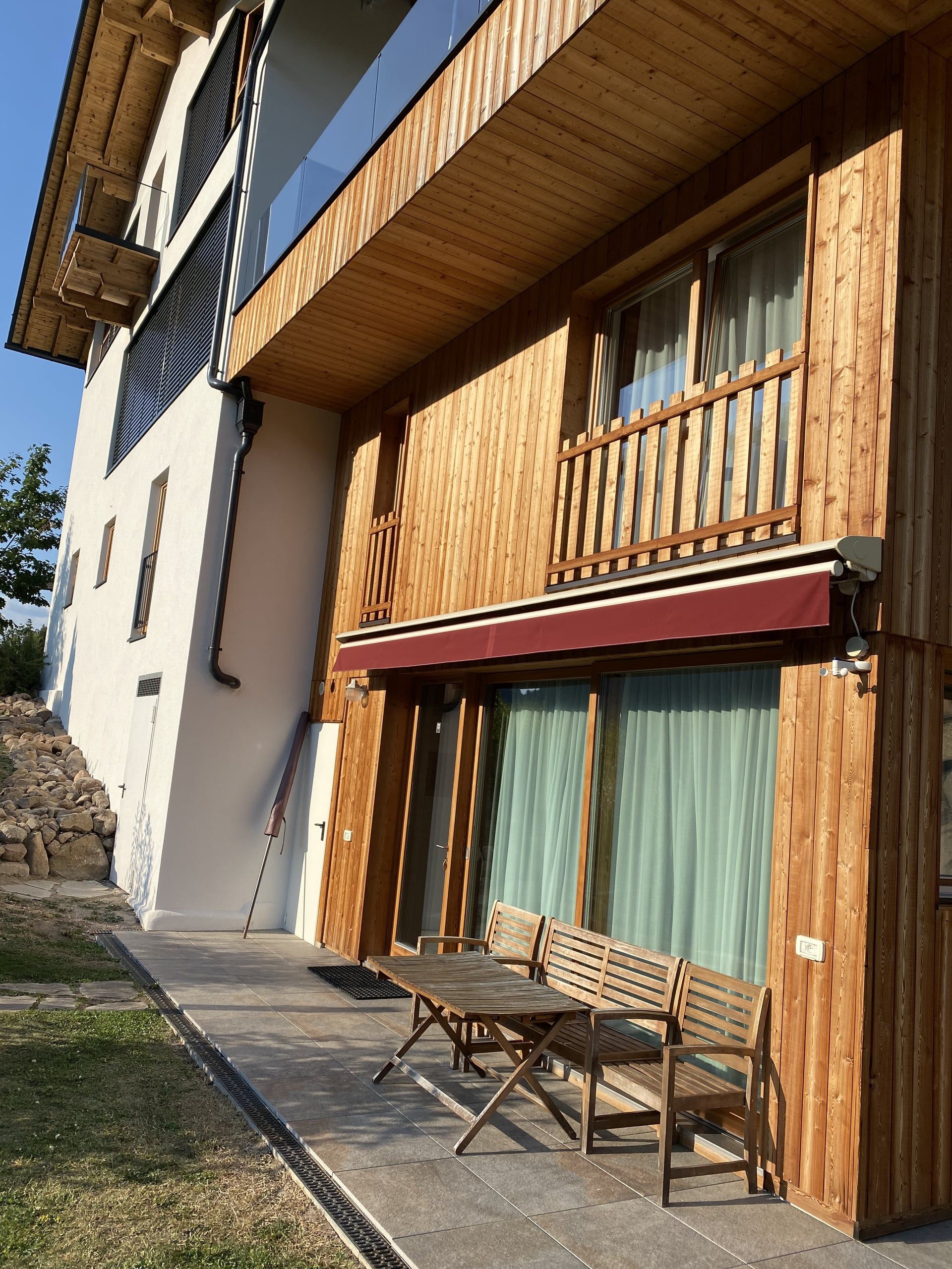 Wooden façade of the Buche apartment with terrace, red awning and garden furniture