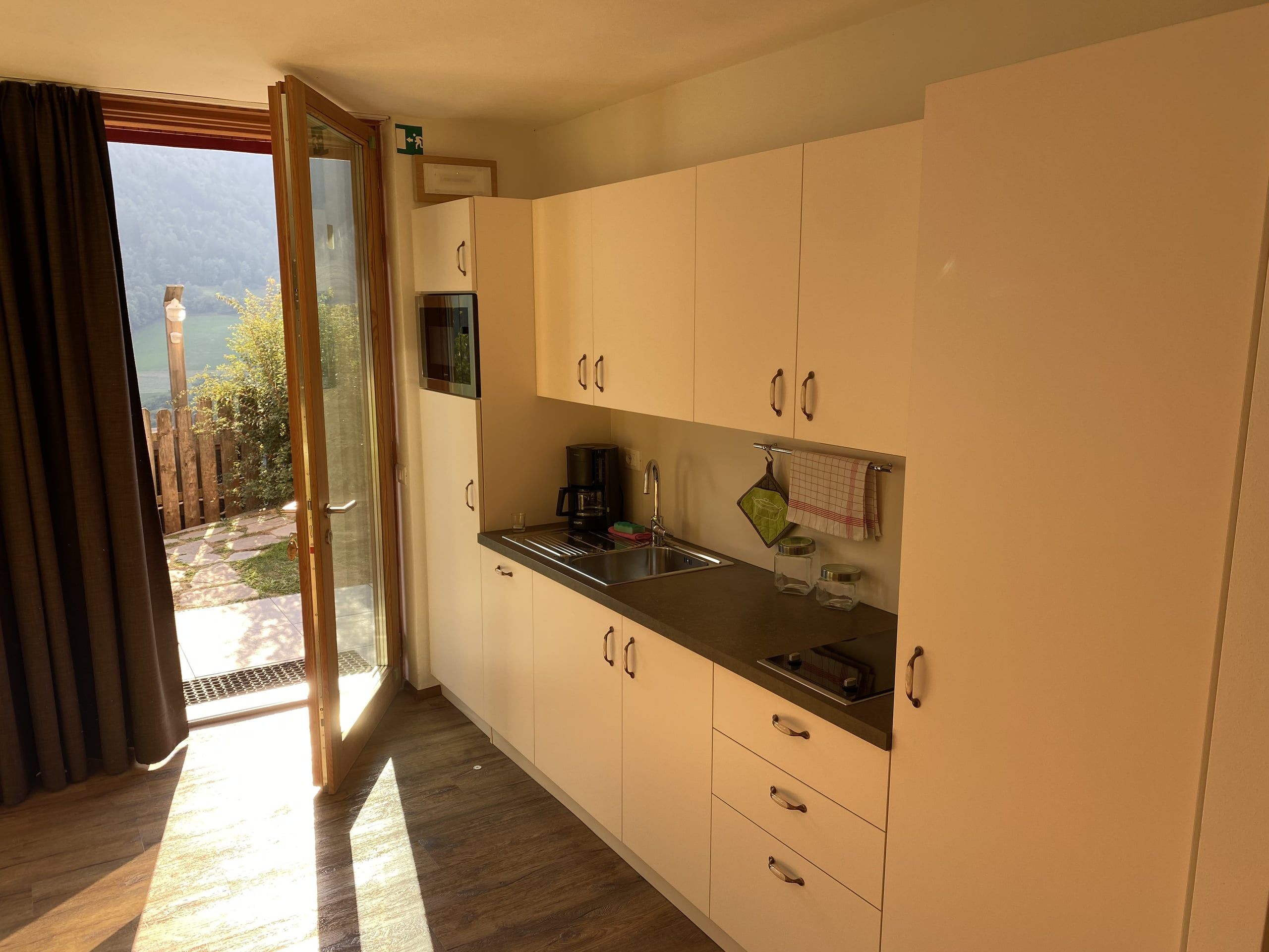Kitchenette with light-coloured units next to the open terrace door in the Buche apartment