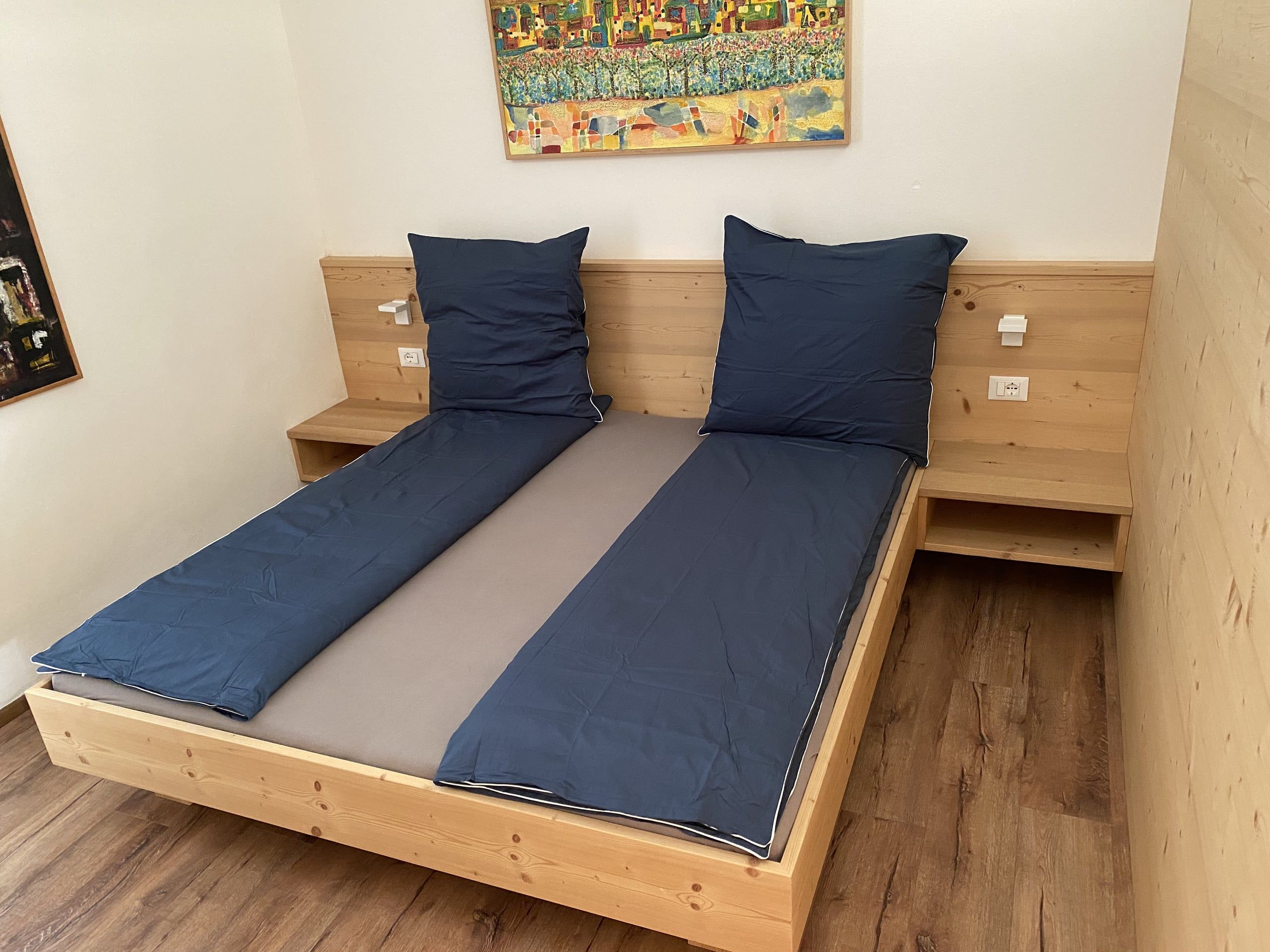 Light wooden double bed with blue bed linen in the bedroom of the Buche apartment