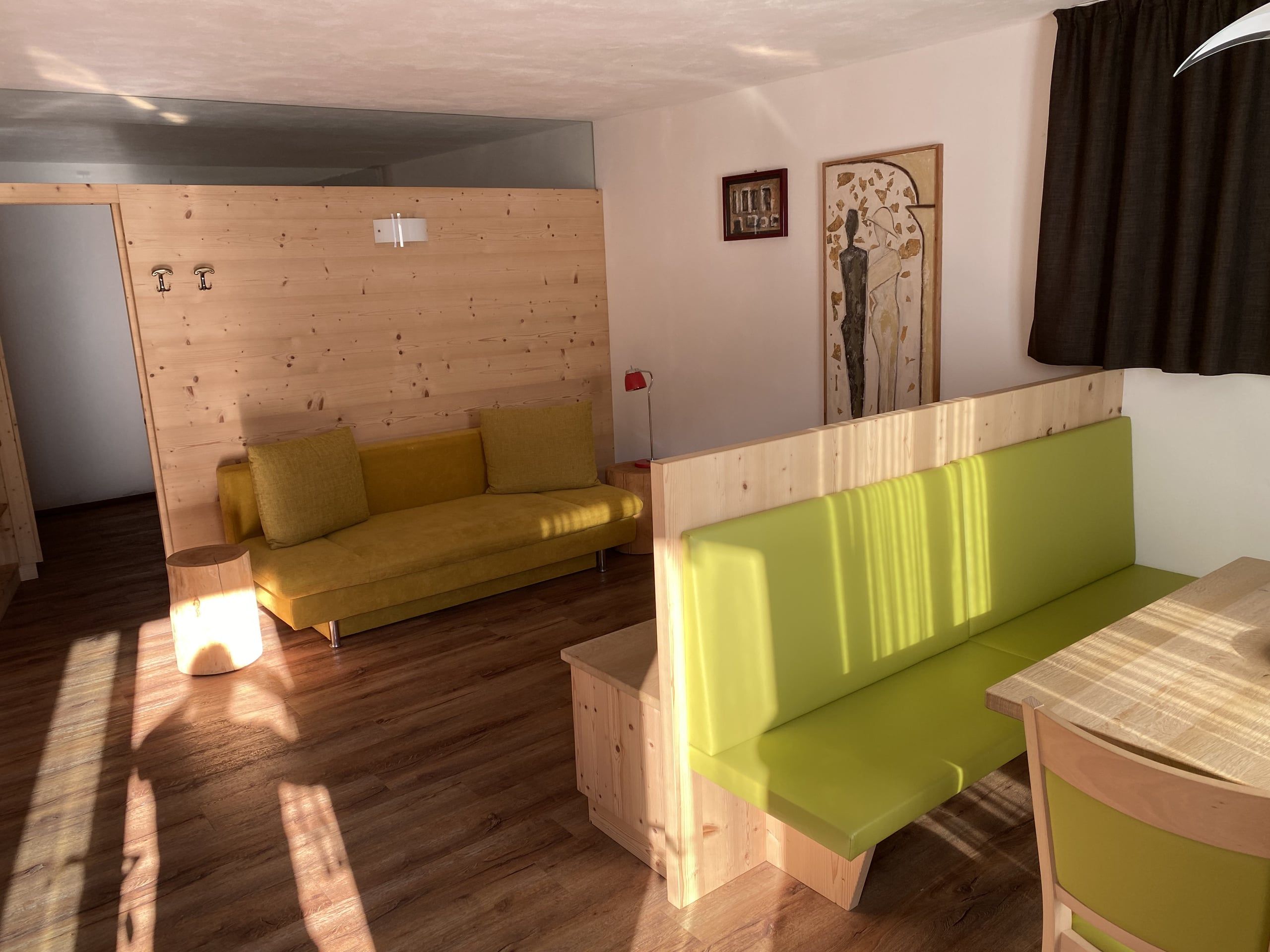 Living room in the Buche apartment with yellow sofa, green corner bench and light wooden room divider