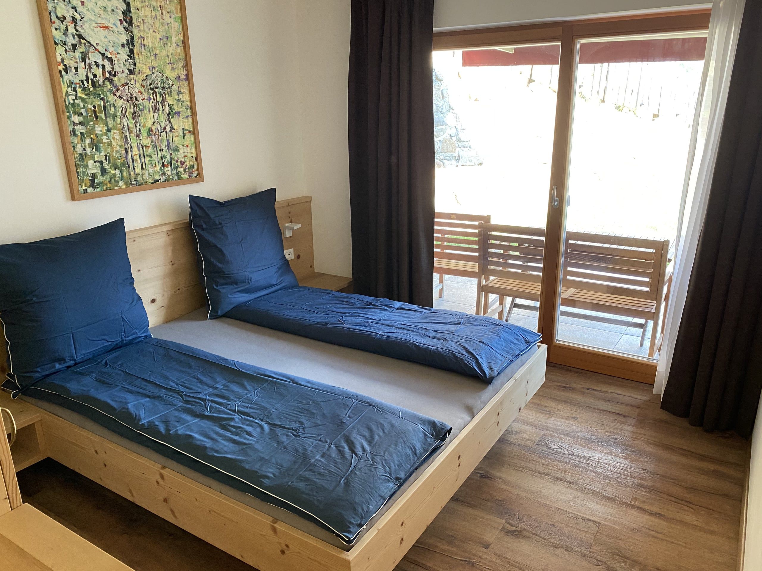 Light wooden double bed with blue bed linen in front of the glass door to the terrace in the Lärche apartment