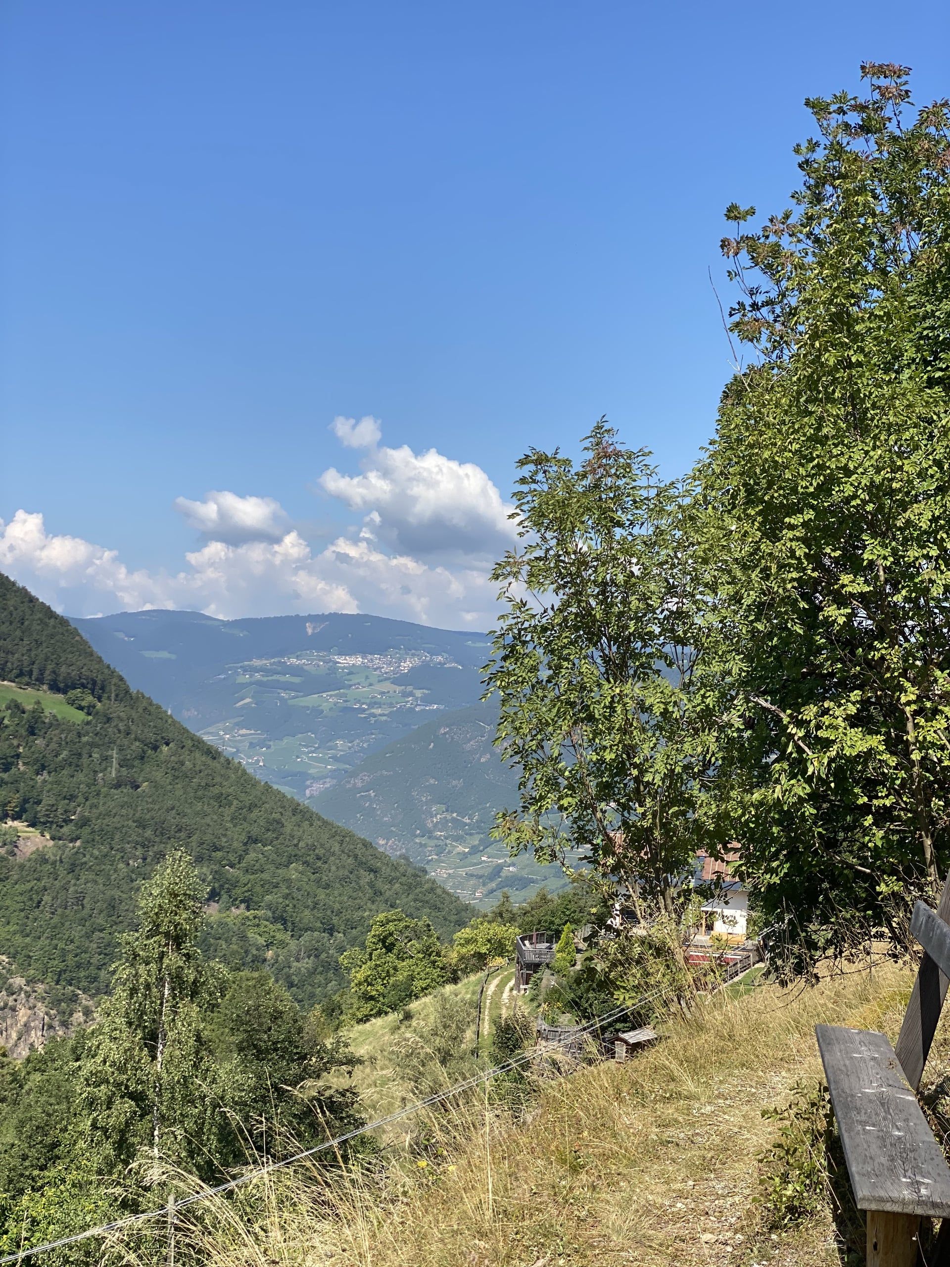 Blick vom Wiesenhang mit Holzbank über das Tal bis zu fernen Bergen