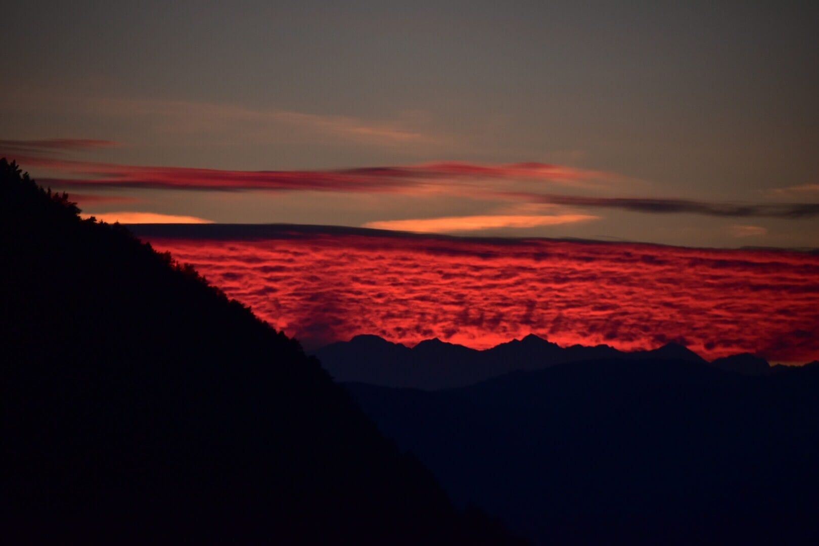 Rot leuchtendes Wolkenmeer im Abendrot hinter dunklen Bergsilhouetten